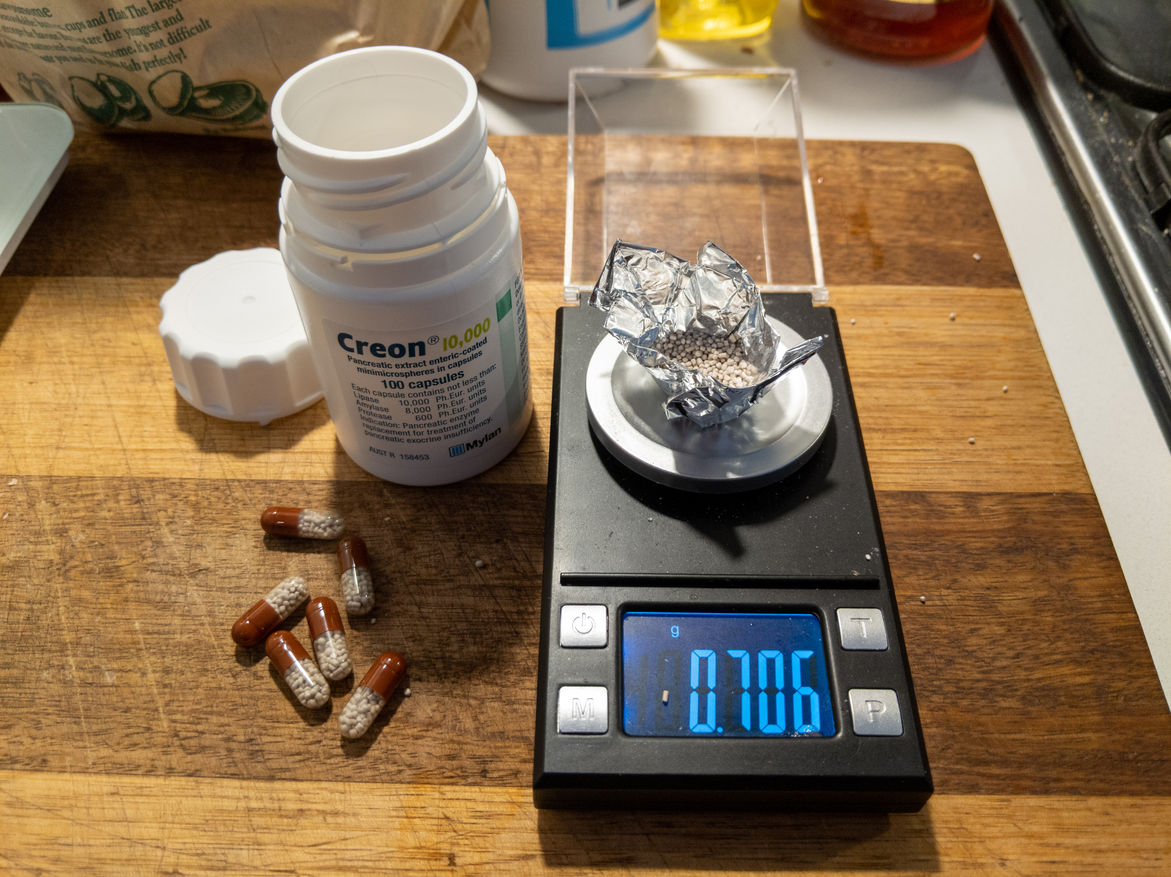 A picture of a small scale with a foil 'boat' on it, with some powder in it. Next to the scale are some gel capsules and a pill bottle